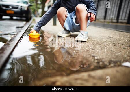 Jungen spielen mit Spielzeugboot auf dem Wasser auf Bürgersteig Stockfoto