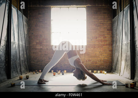 Eine blonde Frau in einem weißen bauchfreies Top und Leggings, bücken zu müssen auf dem Boden, umgeben von Kerzen in einer Yogaposition. Stockfoto