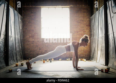 Eine blonde Frau in einem weißen bauchfreies Top und Leggings, bücken zu müssen auf dem Boden, umgeben von Kerzen, Yoga zu tun. Stockfoto