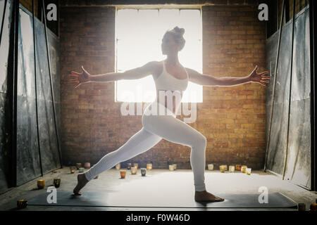 Eine blonde Frau steht auf eine Yoga-Matte, umgeben von Kerzen, machen Yoga, Arme ausgestreckt. Stockfoto