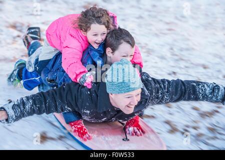 Porträt von Vater, Sohn und Tochter fahren Schlitten bergab übereinander legen Stockfoto