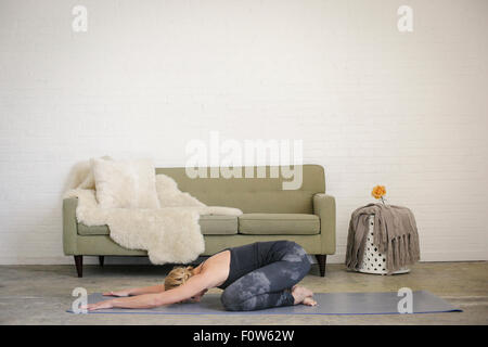 Eine blonde Frau kniend auf eine Yoga-Matte in einem Raum, streckte beim Yoga, Arm vor ihr. Stockfoto