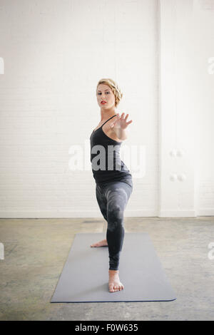 Eine blonde Frau in einem schwarzen Anzug und Leggings biegen Sie ihre Knie in einem Ausfallschritt mit ihren ausgestreckten Armen. Stockfoto