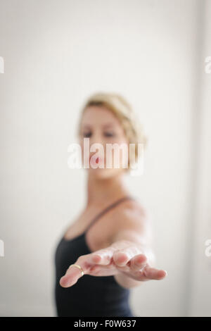 Eine blonde Frau in eine schwarze Trikot in einem Raum stehen, machen Yoga, Arm ausgestreckt. Stockfoto