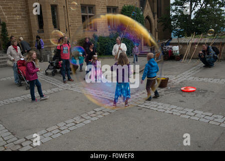 A Street Performer bläst Riesenseifenblasen um Kinder auf der Burg Hohenzollern, Baden-Württemberg, Deutschland Stockfoto