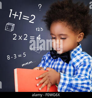 Kleiner Junge im Mathematikunterricht, in Händen Buch halten und stehen in der Nähe von Blackboard mit schriftlichen mathematische Gleichung, zurück zur Schule Stockfoto