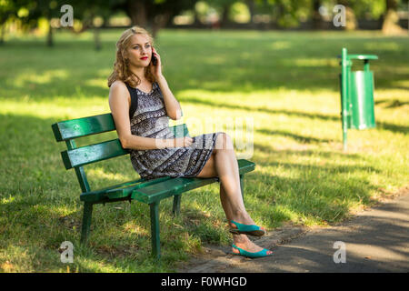 Blonde Frau am Handy sitzen auf einer Bank im Park. Stockfoto