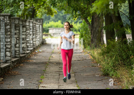 Junge Frau läuft auf der Strecke durch den Sommerpark. Im Freien Training. Training in einem Park. Stockfoto