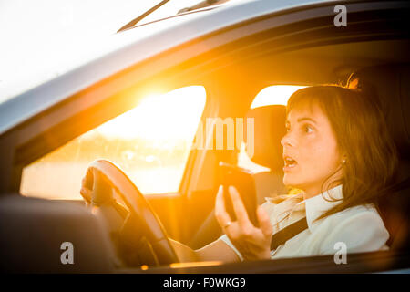 Junge Frau Laufwerke mit Handy in der Hand - riskantes Autofahren Stockfoto