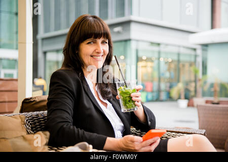 Senior Business-Frau outdoor im street Bar Mojito trinken und auf ihr Handy Stockfoto