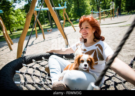 Reife Frau mit ihrem tierischen Freund außerhalb auf Spielplatz Schaukeln Stockfoto