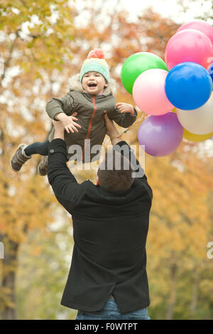 glücklicher Vater werfen kleine Kind mit Luftballons, Ausflug im Herbst park Stockfoto