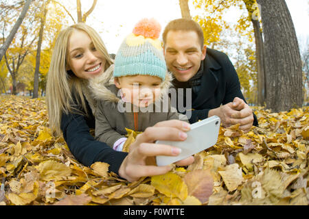 glückliche Familie mit Kleinkind nehmen Selfie am Telefon, im Herbst Park Ausflug Stockfoto