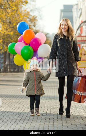 glückliche Frau und Kind mit roten Einkaufstasche und Luftballons, gehen auf der Straße Stockfoto