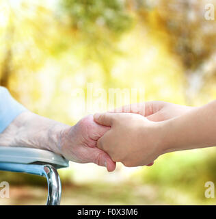 Ältere Frau im Rollstuhl, die Hand in Hand mit jungen Hausmeister im Herbst Stockfoto