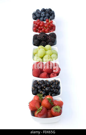 Johannisbeeren, schwarze Johannisbeeren, Brombeeren, Trauben, Erdbeeren, Himbeeren und Heidelbeeren in weißen Schalen auf einem weißen Hintergrund. Stockfoto