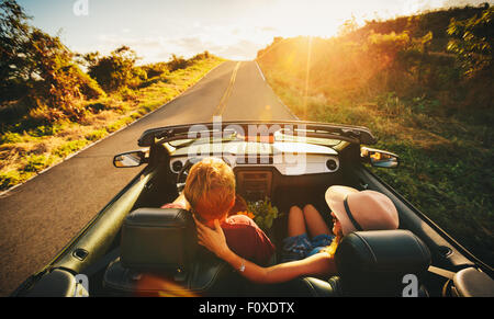 Glückliches junges Paar Fahrt entlang der Landstraße im Cabrio bei Sonnenuntergang Stockfoto
