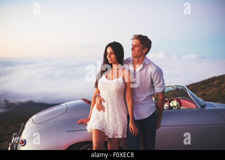 Romantische junge attraktive paar den Sonnenuntergang mit klassischen Oldtimer Sportwagen Stockfoto