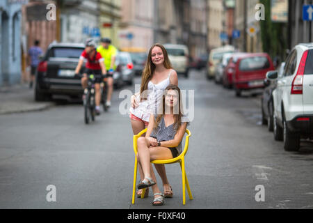 Teenager-Mädchen auf der Straße der Altstadt. Ein Mädchen sitzt auf dem Stuhl auf der Straße, das zweite Mädchen war hinter ihr. Stockfoto