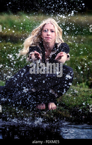eine Frau sitzt an einem Teich und ist mit Wasser Spritzen Stockfoto