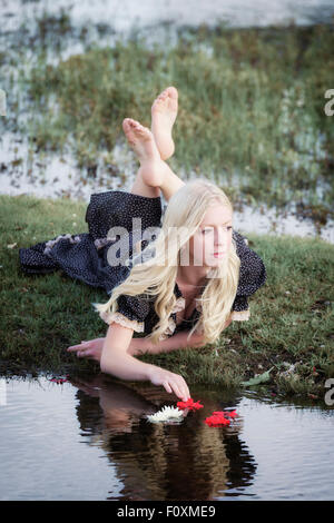 eine Blondine ist Blumen auf einem Teich platzieren.