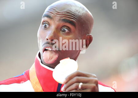 Peking, China. 23. August 2015. Großbritanniens Mohamed Farah steckt seine Zunge heraus, wie er seine Goldmedaille für die Männer zeigt 10 000 M bei den 15. International Association of Athletics Federations (IAAF) Leichtathletik-Weltmeisterschaften in Peking, China, 23. August 2015. Foto: Michael Kappeler/Dpa/Alamy Live News Stockfoto