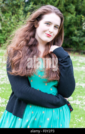 Junge Frau mit einzigartigen braune Augen und braune locken.  Sie ist in einem Feld von Gänseblümchen Stand. Stockfoto