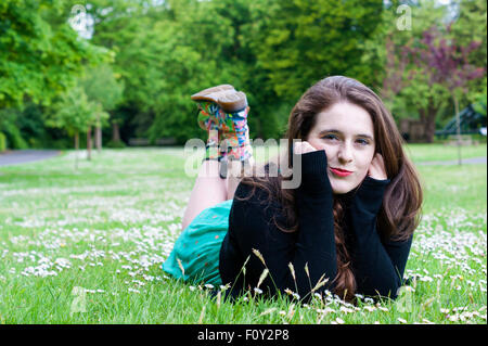 Junge Frau mit einzigartigen braune Augen und braune locken.  Sie liegt auf einem Feld von Gänseblümchen. Stockfoto