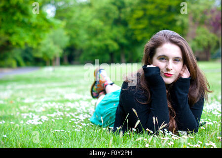 Junge Frau mit einzigartigen braune Augen und braune locken.  Sie liegt auf einem Feld von Gänseblümchen. Stockfoto