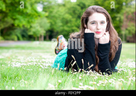 Junge Frau mit einzigartigen braune Augen und braune locken.  Sie liegt auf einem Feld von Gänseblümchen. Stockfoto