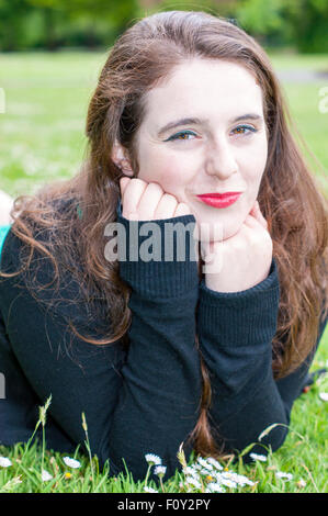 Kopfschuss einer jungen Frau mit einzigartigen braune Augen und braune locken.  Sie liegt auf einem Feld von Gänseblümchen, Stockfoto