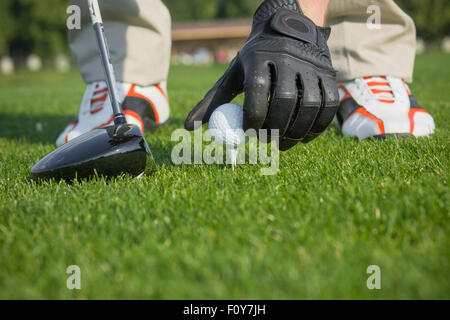 Des Mannes Hand im Lederhandschuh ein t-Stück mit Golfball isoliert auf der grünen Wiese Hintergrund platzieren. Golfball und Stick mit Golfer-le Stockfoto