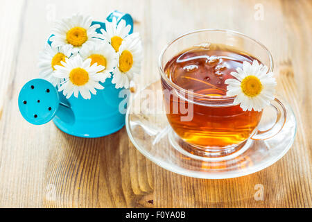 Kamillentee in eine Tasse und Kamille Glasblumen in eine kleine blaue Gießkanne Stockfoto