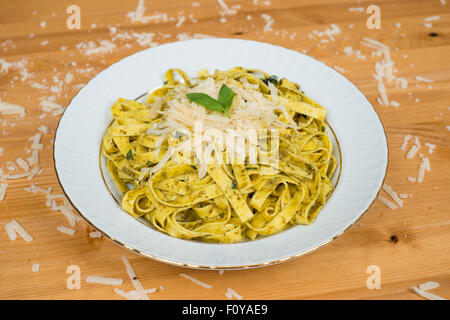 Tagliatelle Nudeln mit Pesto und Basilikum Blätter auf weißen Teller, Holz Hintergrund Stockfoto