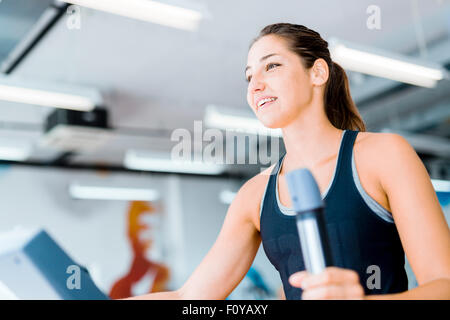 Schöne junge Dame mit dem elliptischen Trainer in einem Fitnessstudio in eine positive Stimmung Stockfoto
