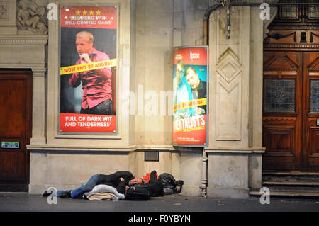 London, UK, 21.08/2015, ein Obdachloser schläft unter der Bandenwerbung auf der Straße vor dem Wyndham Theatre in Charing Cross Road in der Nähe der u-Bahn-Station Leicester Square im Londoner West End. Stockfoto