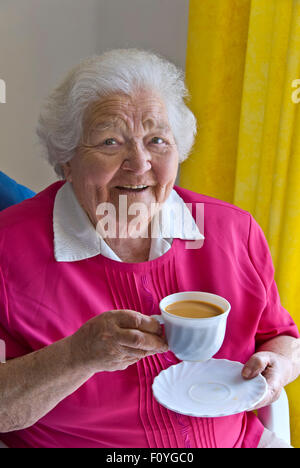 Glücklich Content senior ältere Dame mit einer Tasse Tee zu Hause in ihrem hellen luftigen Zimmer sitzen Stockfoto