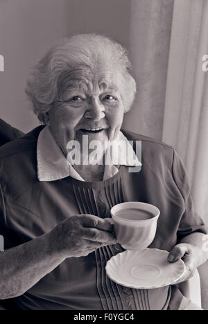 B&W RGB Konvertierung Bild glücklich zufriedenen senior alte ältere Dame mit einer Tasse Tee zu Hause zu sitzen. Stockfoto
