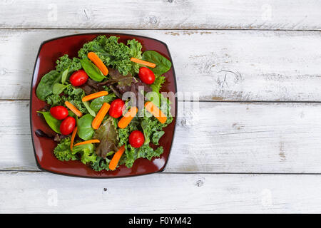 Hoher seitlicher Blick auf frischem grünen Salat mit Karotten, Cherry-Tomate, Basilikum, Baby Grünkohl und Salat auf rustikalen hölzernen Tafeln. Stockfoto