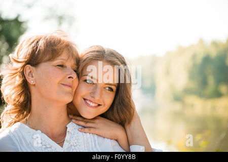 Reife Mutter umarmt mit Teen Tochter in der Natur im Freien an sonnigen Tag Stockfoto