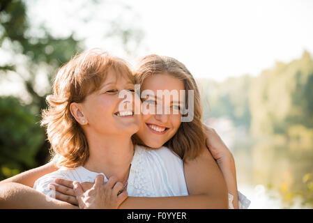 Reife Mutter umarmt mit Teen Tochter in der Natur im Freien an sonnigen Tag Stockfoto