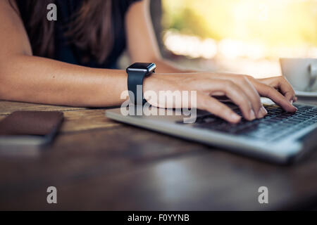 Händen der Trägerin Smartwatch auf der Tastatur ihres Notebook-PCs. Frauen arbeiten am Laptop in einem Café. Stockfoto