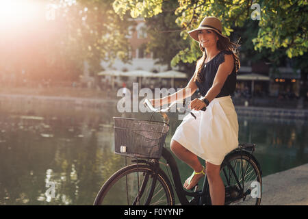 Porträt von attraktiven jungen Frau, die mit dem Fahrrad an einem Teich im Stadtpark an einem Sommertag. Stockfoto