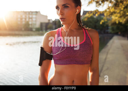 Junge Frau Läufer Armbinde tragen und Musik über Kopfhörer hören. Passen Sie die Sportlerin, die eine Pause von im freien training. Stockfoto