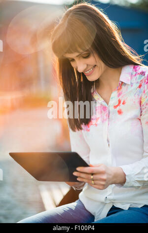 Junge schöne Frau sitzt auf der Bank in der Straße und das Surfen Internet Tablet