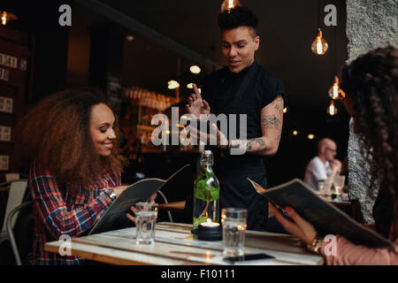 Glückliche junge Menschen sitzen im Restaurant Speisekarte lesen und Befehle zu erteilen, dem männlichen Kellner beim Kellner setzen auf Stockfoto