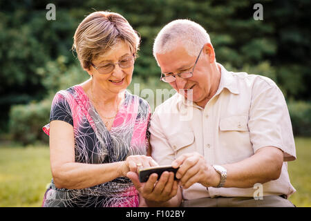 Älteres Paar suchen gemeinsam auf Fotos in Smartphone - draußen in der Natur Stockfoto