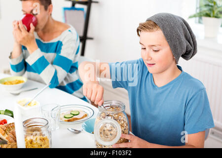 Mutter und Sohn zusammen mit Frühstück am Morgen. Sohn mit Getreide aus einer Flasche am Frühstückstisch. Stockfoto