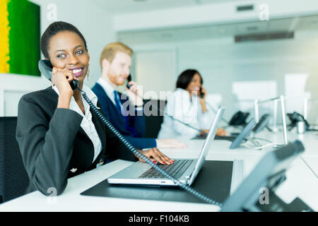 Eine schöne, schwarze, junge Frau arbeitet in einem Callcenter in einem Büro mit ihrem roten Haird Partner am anderen Ende des Schreibtisches ta Stockfoto