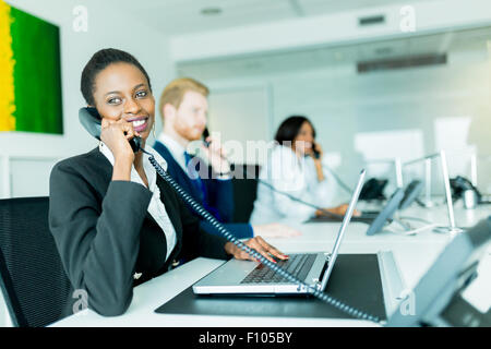 Eine schöne, schwarze, junge Frau arbeitet in einem Callcenter in einem Büro mit ihrem roten Haird Partner am anderen Ende des Schreibtisches ta Stockfoto